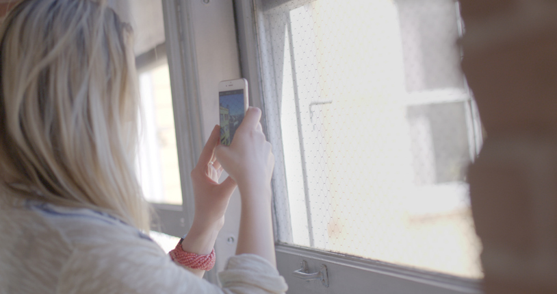 OTS attractive blonde girl taking pictures through window on phone